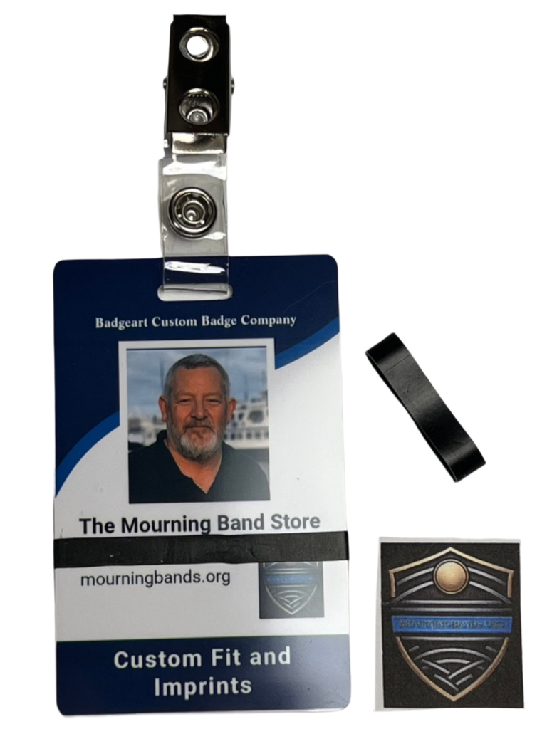 A photo of a blue employee identification badge for Badgeart Custom Badge Co. with a black silicone mourning band attached. An unattached band is shown next to the badge, demonstrating how to wear a mourning band on a public safety civilian employee ID to mourn a coworker's death.