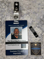 A photo of a blue employee identification badge for Badgeart Custom Badge Co. with a black silicone mourning band attached. An unattached band is shown next to the badge, demonstrating how to wear a mourning band on a public safety civilian employee ID to mourn a coworker's death.